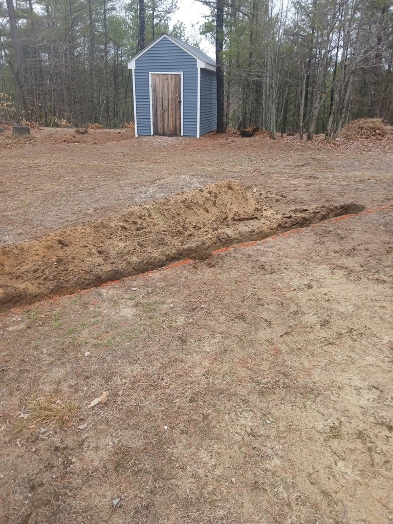 Small blue and brown shed with wooden door in wooded clearing with dirt ground and trenches
