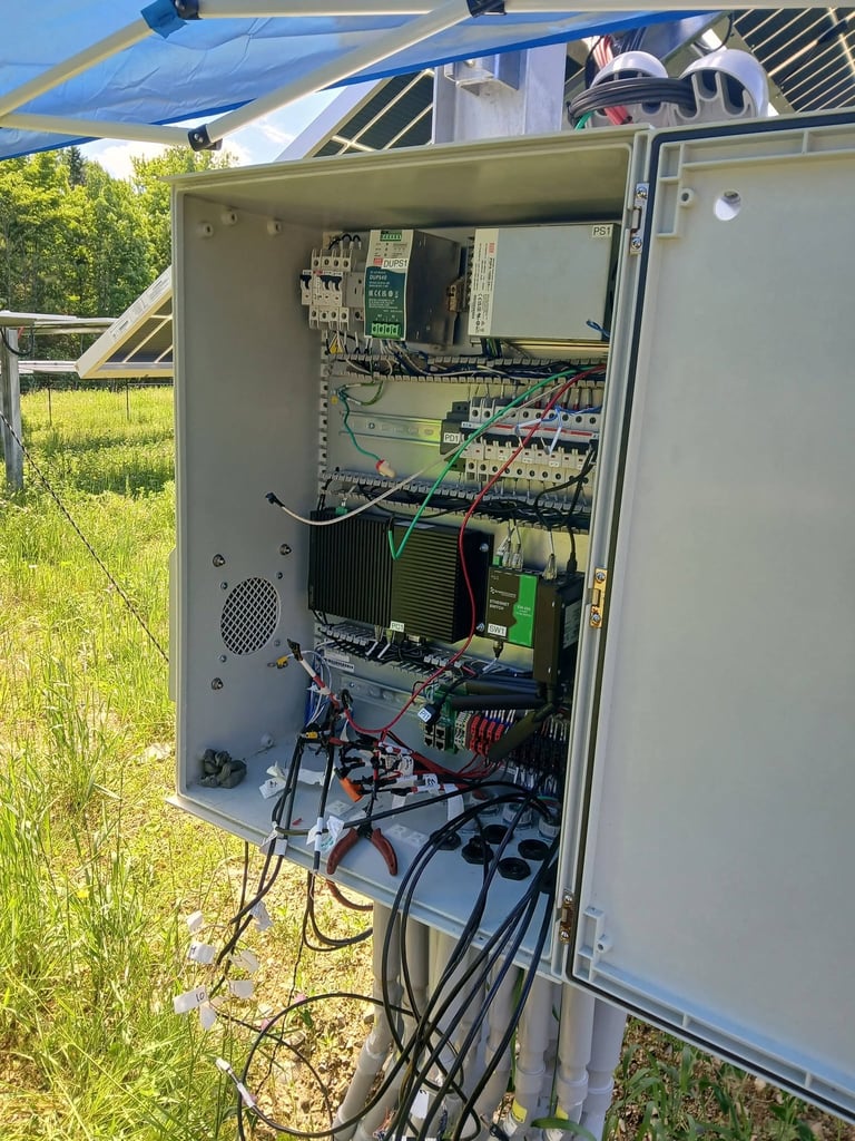 Open electrical control panel with circuit breakers, wiring, and components mounted on interior wall in outdoor setting